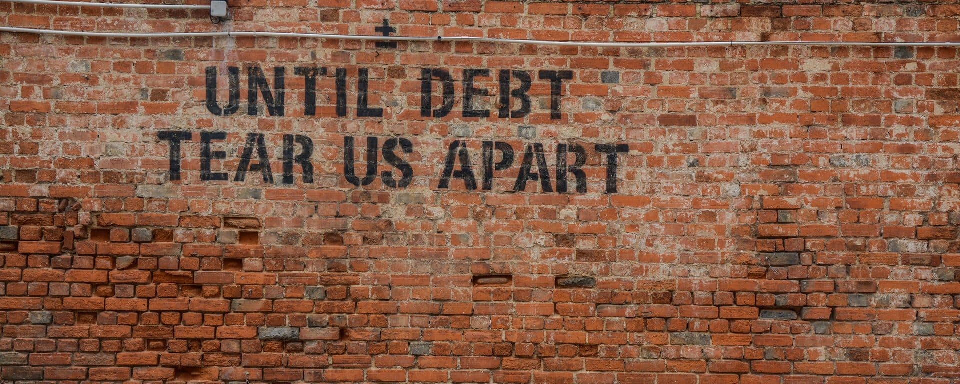 Brick wall painted with the words Until debt tear us apart