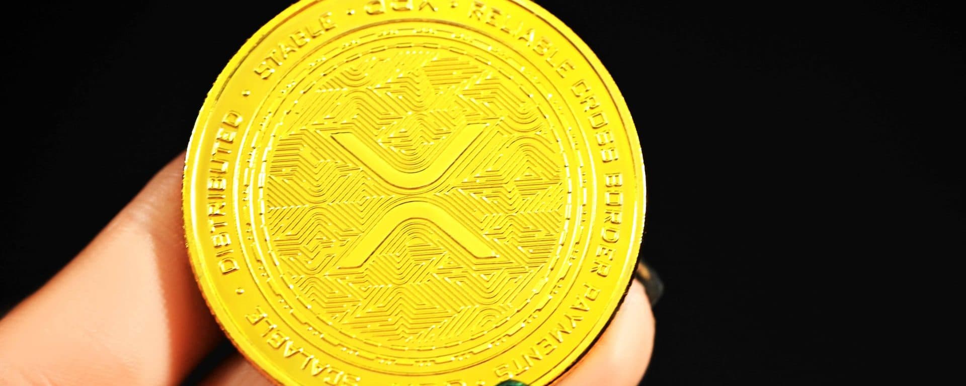 Gold-colored XRP token held between two fingers