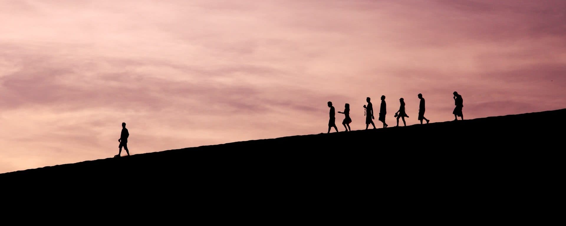 Silhouettes of people following a leader uphill at sunset