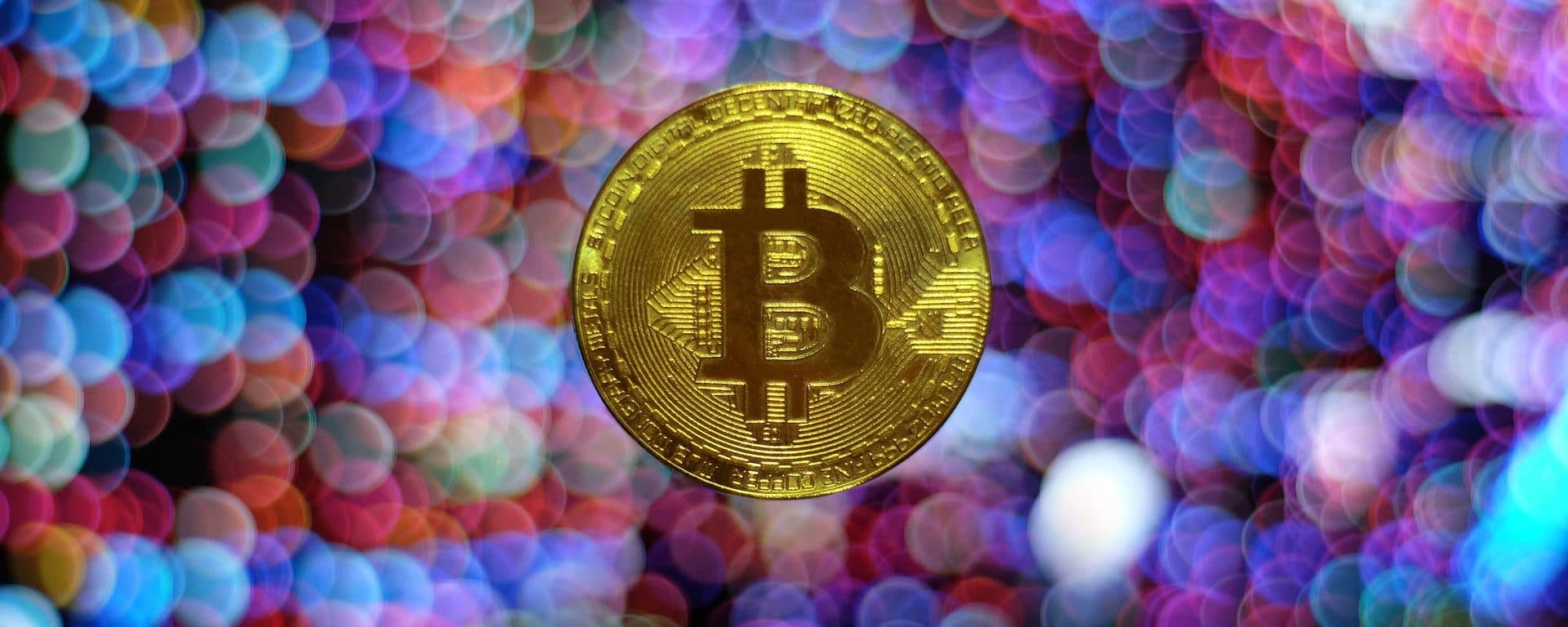 Gold-colored Bitcoin token against blurred multicolored lights