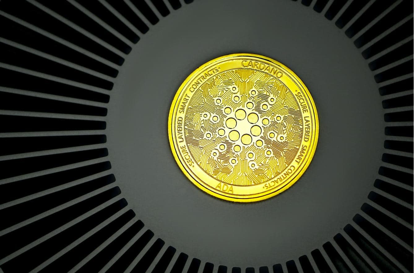 Gold-colored Cardano token on a dark patterned surface