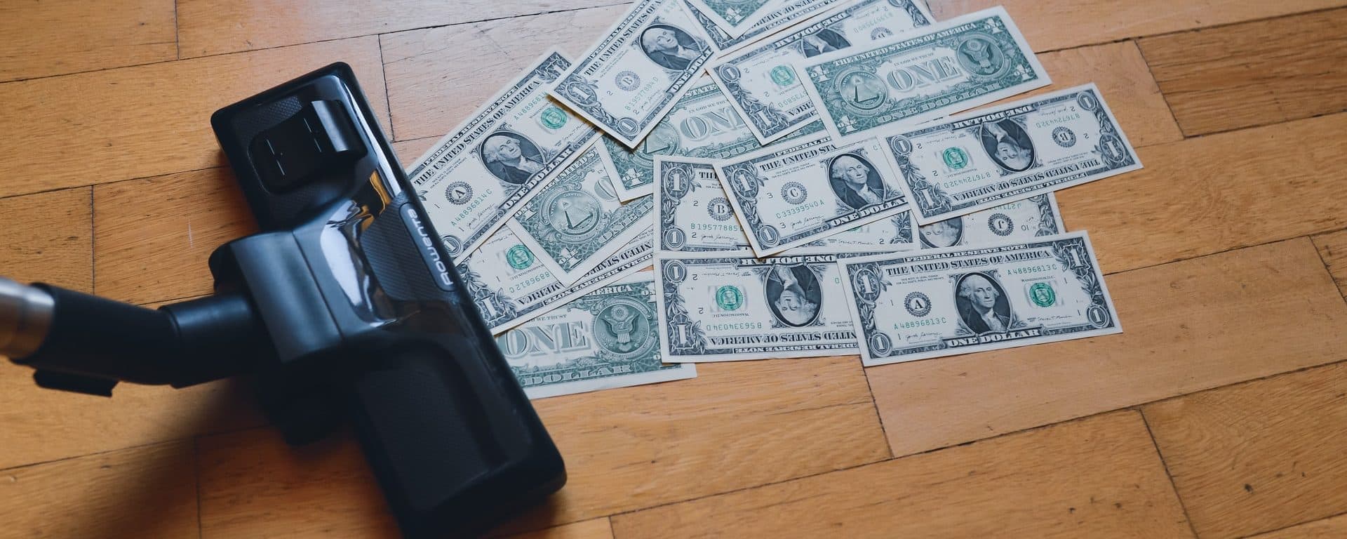 Vacuum cleaner beside scattered U.S. dollar bills on a wooden floor
