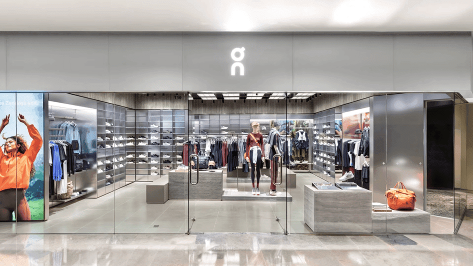 Exterior of an On store with shoe wall, apparel racks and mannequins, and a Zendaya campaign poster on the left.